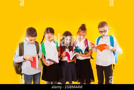 Fröhliche lächelnde kleine Studenten halten Farbbücher isoliert auf gelbem Hintergrund. Zurück zur Schule. Stockfoto