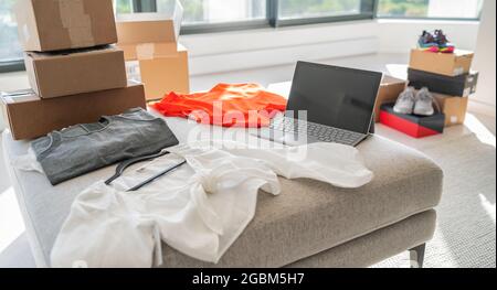 Online-Shop Verkauf neuer Kleidung von zu Hause. Kleinunternehmen, die an Laptops für Modebekleidung arbeiten, die in Versandkartons geliefert wird Stockfoto