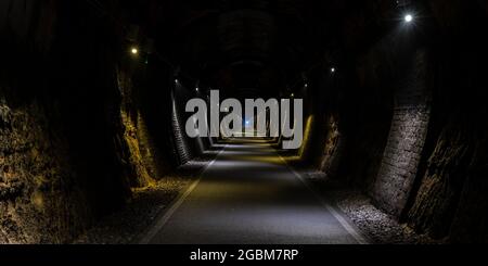 Im dunklen Combe Down Tunnel, Teil der beiden Tunnel Greenway Rail Trail in Bath, Somerset, leuchtet ein Radfahrerscheinwerfer. Stockfoto