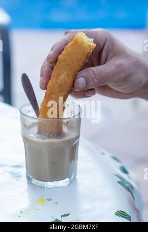 Vertikale Aufnahme einer männlichen Hand, die ein Stück Keks in ein Glas mit heißem Getränk einweicht Stockfoto