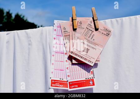 Britische nationale Lotterie-Tickets und rutscht auf Wäscheleine mit Haken auf blauem Himmel Hintergrund. Stockfoto