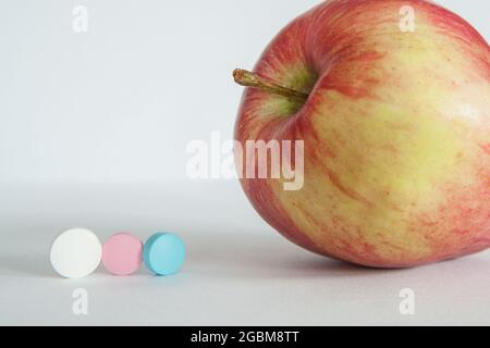 Roter Apfel oder Vitamintabletten auf hellgrauem Hintergrund. Gesunde Ernährung, Ernährung, Lifestyle-Konzept, Behandlung Wahl Konzept. Hochwertige Fotos Stockfoto