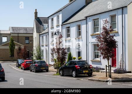 Straßenbäume markieren Parkplätze auf der Straße vor den neu erbauten Häusern in der neuen Stadt Poundbury, Dorset. Stockfoto