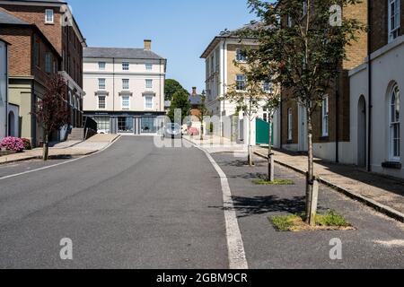 Straßenbäume markieren Parkplätze auf der Straße vor den neu erbauten Häusern in der neuen Stadt Poundbury, Dorset. Stockfoto