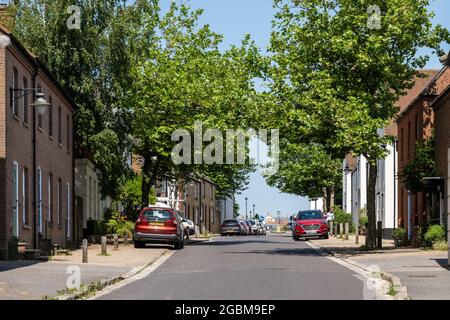 Große Straßenbäume und geparkte Autos füllen das Straßenbild der Middlemarsh Street, einer der ersten Straßen, die in der neuen Stadt Poundbury, Dorset, gebaut werden. Stockfoto