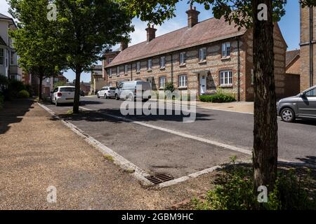 Straßenbäume markieren Parkplätze auf der Straße vor traditionellen, neu erbauten Häusern in der neuen Stadt Poundbury, Dorset. Stockfoto