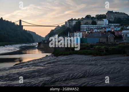 Bei Ebbe geht die Sonne hinter der Clifton Suspension Bridge und dem Stadtbild von Bristol an der Mündung des Flusses Avon unter. Stockfoto