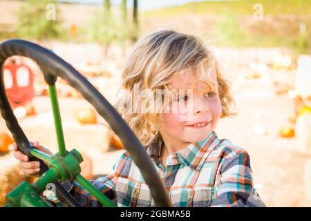 Kleiner Junge, der Spaß in EINEM Traktor in einer rustikalen Ranch-Umgebung im Pumpkin Patch hat. Stockfoto