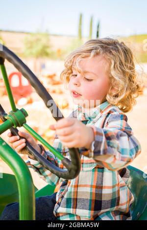 Kleiner Junge, der Spaß in EINEM Traktor in einer rustikalen Ranch-Umgebung im Pumpkin Patch hat. Stockfoto