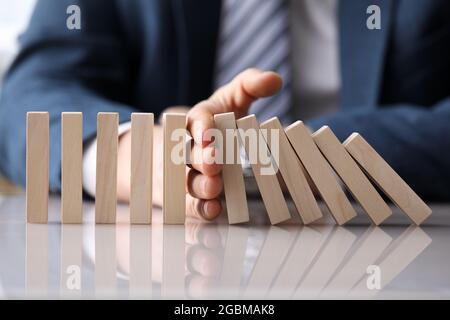 Geschäftsmann im Anzug hält mit der Hand fallen Folge Holzblöcke Stockfoto
