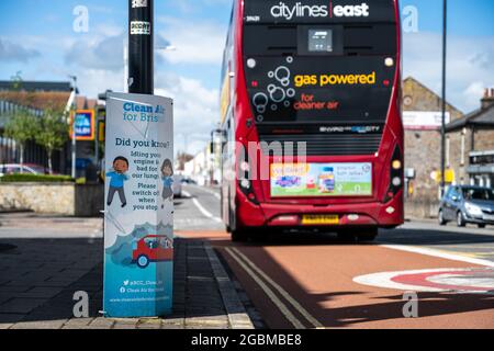 Ein Biogas-Bus fährt an einem „Clean Air“-Plakat vorbei, auf dem die Autofahrer aufgefordert werden, ihre Motoren im Leerlauf an einer Kreuzung an der Fishponds Road in Bristol abzuschalten. Stockfoto