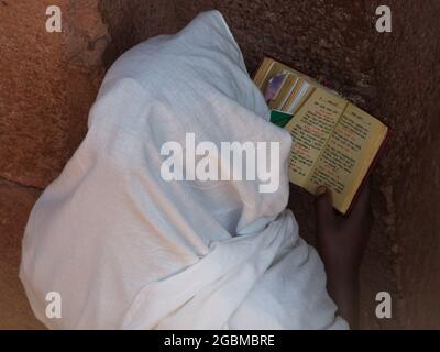 Nahaufnahme Porträt eines Priesters, der die bibel in einer unterirdischen, in Felsen gehauenen Kirche im UNESCO-Weltkulturerbe Lalibela, Äthiopien liest. Stockfoto