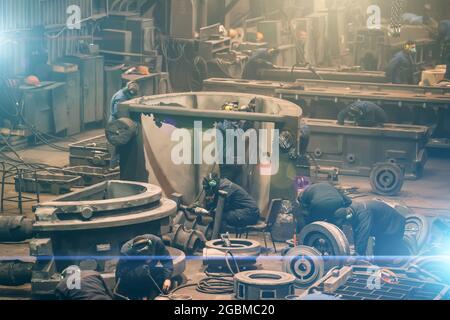 Metallurgische Werkstätte mit vielen Arbeitern, die mit Gusseisen-Teilen arbeiten, Postgußverarbeitung in der Gießerei der Stahlfabrik, Blick von oben. Stockfoto