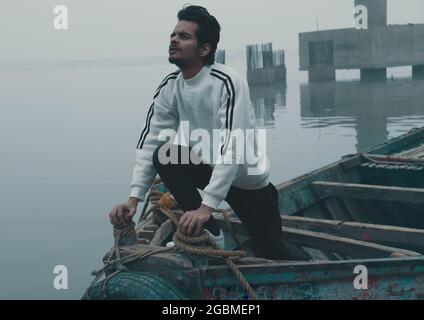 Junger asiatischer Mann posiert an einem düsteren Tag dramatisch in einem Boot Stockfoto