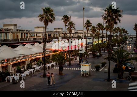 Zwei Frauen gehen nach einem stürmischen Tag in der Stadt an den fast leeren Terrassen der Bars und Restaurants des Port Olimpic in Barcelona vorbei. Stockfoto