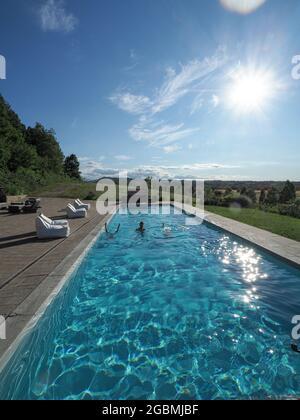 Vertikale Aufnahme eines kaukasischen Mannes im Pool mit zwei kopfüber stehenden Frauen an einem sonnigen Tag Stockfoto