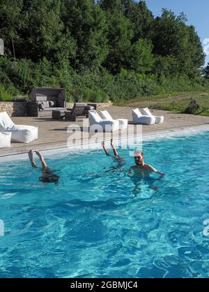 Vertikale Aufnahme eines kaukasischen Mannes im Pool mit zwei kopfüber stehenden Frauen an einem sonnigen Tag Stockfoto