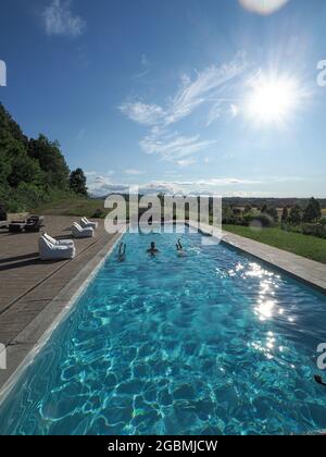 Vertikale Aufnahme eines kaukasischen Mannes im Pool mit zwei kopfüber stehenden Frauen an einem sonnigen Tag Stockfoto