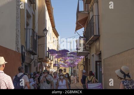 BRIHUEGA, SPANIEN - 10. Jul 2021: Viele Menschen, die durch die Straßen mit lila Regenschirmen über ihnen Stockfoto