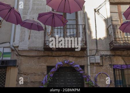 BRIHUEGA, SPANIEN - 10. Jul 2021: Die Reihen der purpurnen Schirme in den engen Straßen von Brihuega Stockfoto