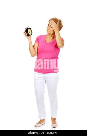 Ganzkörperaufnahme einer besorgten alten polnischen Frau, die ihren Wecker in weiß gehalten hat Stockfoto