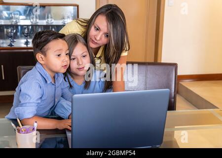 Eine Mutter mit ihrem männlichen Kind und ihrer weiblichen Tochter schaut sich den Computer im Esszimmer an, um online Hausaufgaben zu machen Stockfoto