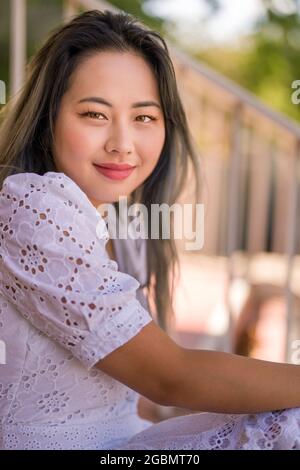 Porträt einer jungen asiatischen Frau in einem weißen Sommerkleid auf der Treppe sitzend Stockfoto