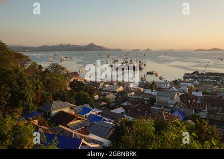 Sonnenuntergang über der Stadt und dem Hafen von Labuan Bajo, mit vielen traditionellen Phinisi-Kreuzfahrtbooten vor Anker, da die Stadt der Eintrittspunkt zum Komodo National ist Stockfoto