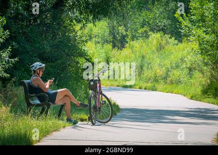 Die Fahrradfahrerin genießt den Sommertag, macht eine Pause vom Reiten, nutzt ihr Handy auf dem East Plum Creek Trail, Castle Rock Colorado US. Foto im Juli. Stockfoto