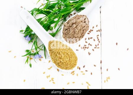 Leinenkleie und Mehl in zwei Löffeln, Samen auf dem Tisch, Leinenblätter und Blumen auf dem Hintergrund der Holzplatte von oben Stockfoto