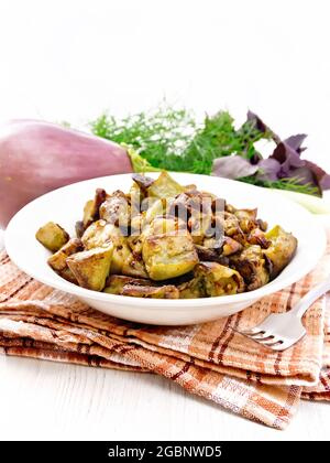 Aubergine gebraten mit Zwiebel, Ei und Gewürzen auf einem Teller auf Serviette, Basilikum, Lauch und Dill auf hellem Holzbrett Hintergrund Stockfoto