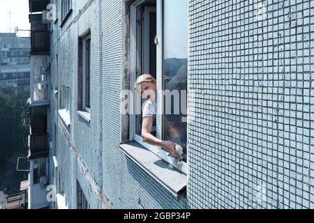 Eine Frau wäscht ein Fenster in einem Hochhaus draußen, Stockfoto