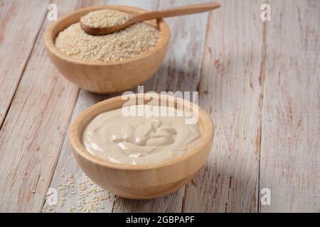 Tahini und Sesam in Holzschüsseln auf Holztisch. Stockfoto