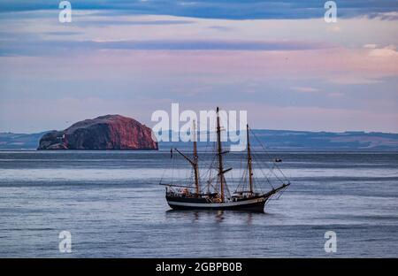 Firth of Forth, Schottland, Großbritannien, 5. August 2021. Sonnenaufgang: Das Hochschiff Pelican aus London, ein quadratischer Rigger der Klasse A, ist vor der Küste von Dunbar mit Blick auf den Bass Rock bei Sonnenaufgang vor Anker gegangen. Das Schiff befindet sich auf der letzten Etappe einer Tour durch Großbritannien Stockfoto