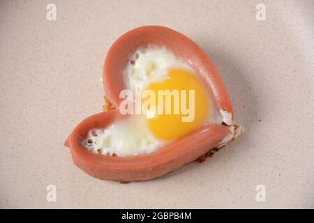 Zwei Würstchen in herzförmigen Spiegelei auf weißem Teller. Frühstück am Valentinstag Stockfoto
