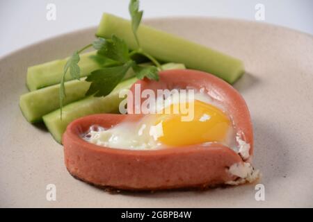 Zwei Würstchen in einem herzförmigen Spiegelei mit grünen Gurken. Frühstück am Valentinstag Stockfoto