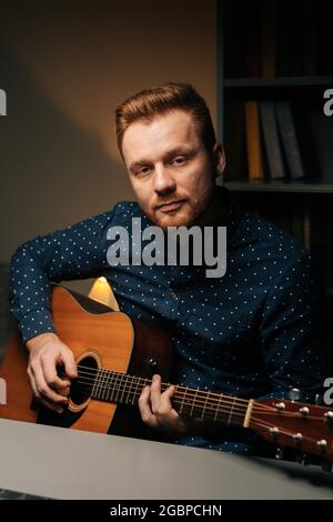 Vertikales Porträt eines ernsthaften Gitarristen Sänger Mann spielen auf akustische Gitarre Aufnahme singen Lied mit professionellen Mikrofonständer in dunklen Home Studio. Stockfoto