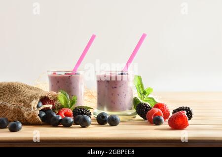 Waldbeerjoghurt Smoothie in Gläsern auf Holztisch mit Sack voller Heidelbeeren, Brombeeren Himbeeren weißen isolierten Hintergrund Stockfoto