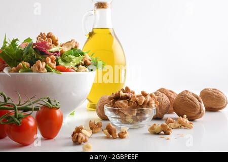Mediterraner Salat mit Walnüssen in einer Schüssel mit Salattomaten und Zwiebeln und Olivenöl auf einem weißen Tisch isoliert Hintergrund. Vorderansicht. Stockfoto