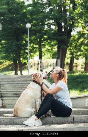 Die blonde Frau spielt während eines Spaziergangs auf einer Treppe im Park mit ihrem goldenen Retriever Stockfoto