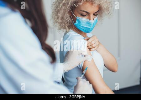 Die blonde Frau wird in einem Gesundheitszentrum mit einer medizinischen Maske geimpft Stockfoto