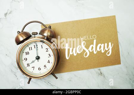 „Hello Tuesday“-Schriftzug auf Papierkarte mit Wecker auf Marmorhintergrund Stockfoto