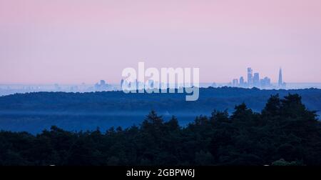 Von der Spitze des Leith Hill auf den Surrey Hills im Südosten Englands aus hat man einen Blick in die Londoner Skyline im Morgengrauen während des Sonnenaufgangs im Juli Stockfoto