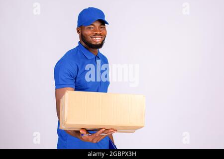 afrikanischer Lieferarbeiter, der eine Geste eines Pakets an einen Kunden übergibt, mit einem Lächeln auf dem Gesicht Stockfoto