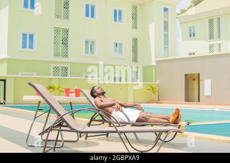 Junger schwarzer Mann, der sich an einem sonnigen Tag am Pool entspannen kann Stockfoto