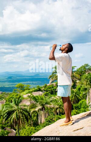 afrikanischer Tourist trinkt Wasser, nachdem er einen Felsen besteigen hat Stockfoto