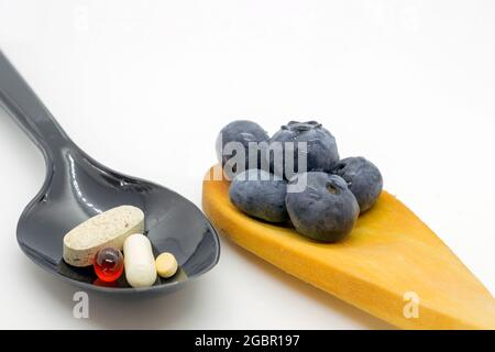 Plastiklöffel mit Drogen und Holzlöffel mit Brombeeren auf weißem Hintergrund. Konzept für ein gesundes Leben Stockfoto