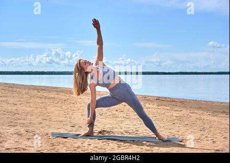 Frau am Strand an einem Sommertag ist in körperlichen Übungen vor dem Hintergrund des Flusses, Yoga, beschäftigt Stockfoto