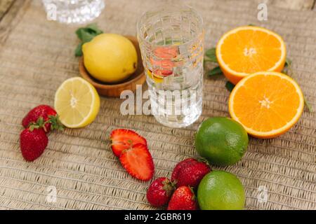 Eine hohe Glastasse aus Wasser mit Eis. In Scheiben geschnittene Orangen, Zitronen, Limetten und Erdbeeren Stockfoto