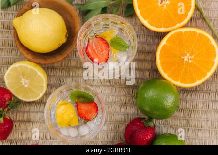Draufsicht auf zwei große Gläser mit Wassereis und Erdbeere. Scheiben frisches Obst auf dem Tisch im Freien. Limette, Zitrone und Orange. Lebensmittelkonzept Stockfoto